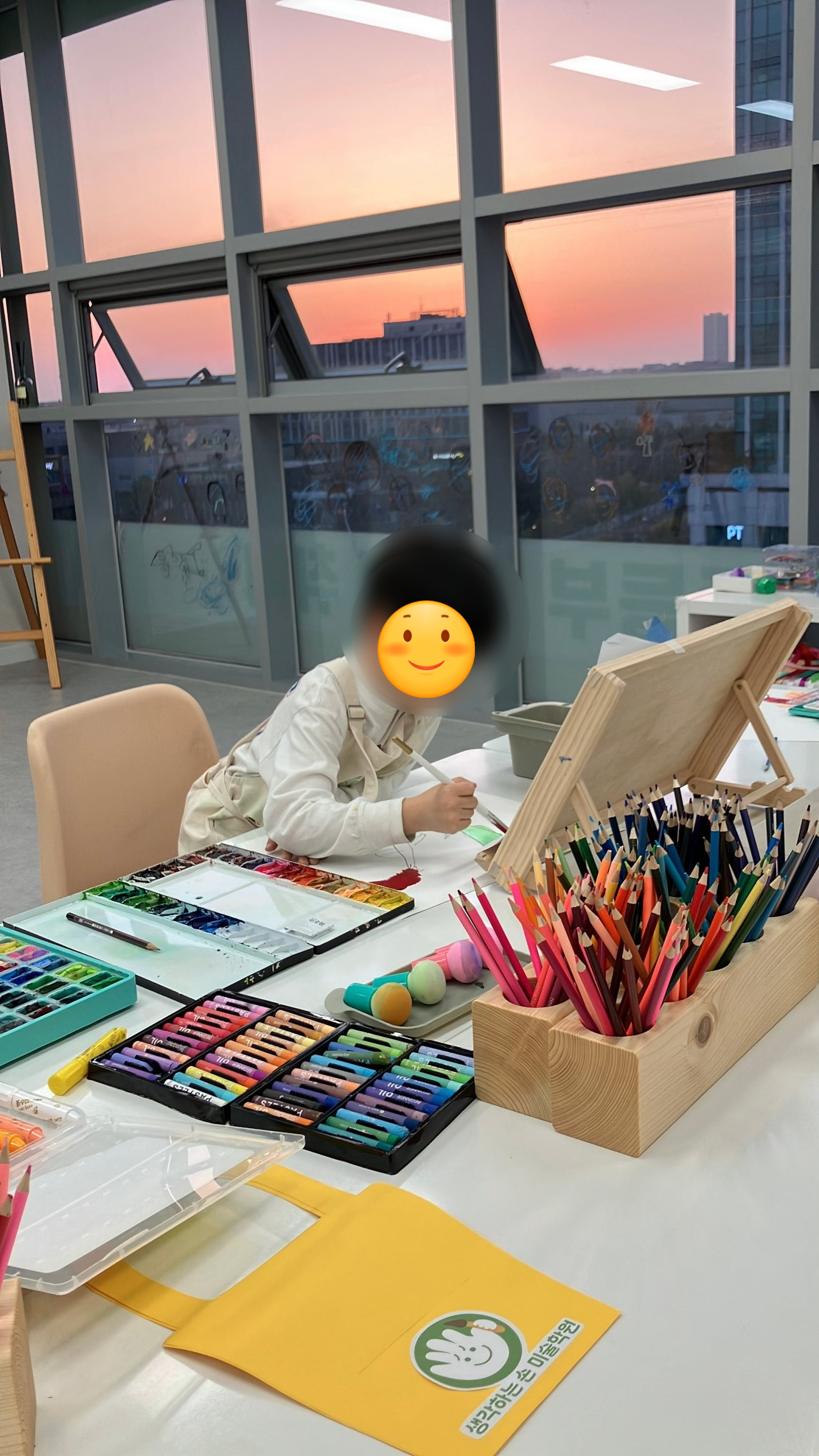 석양이 비치는 창가에서 학생이 색연필로 그리는 모습